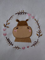 Machine embroidery design with a playful hippopotamus applique surrounded by curving branches in a real