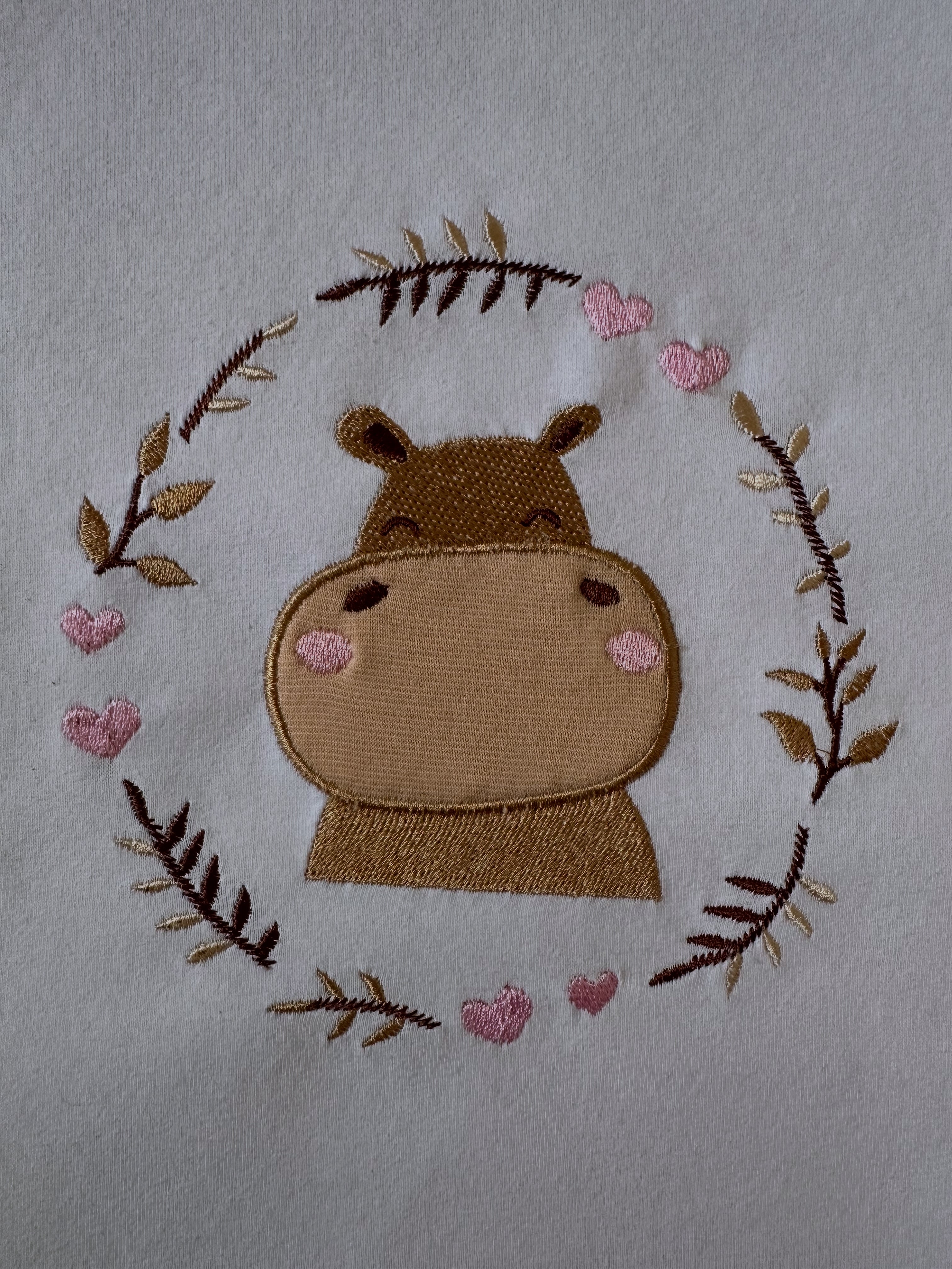 Machine embroidery design with a playful hippopotamus applique surrounded by curving branches in a real